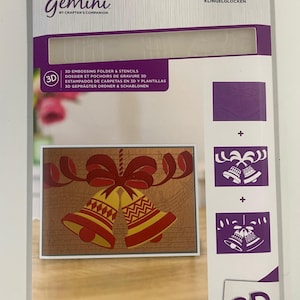 May include: A Gemini 3D embossing folder and stencil set. The package features a design of red and yellow Christmas bells with a red bow. The package dimensions are 5" x 7" (12.7cm x 17.8cm).