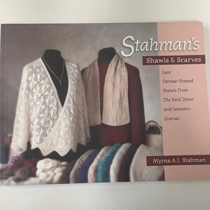 Op de afbeelding: De boekomslag van "Stahman's Shawls & Scarves" toont gebreide sjaals en sjaals. Het toont een witte kanten sjaal en een beige sjaal op mannequins, evenals een verscheidenheid aan kleurrijk garen en gebreide items.