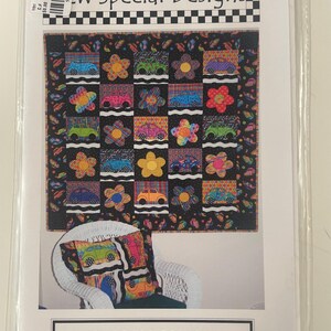 May include: A package for "New Special Designs" featuring a quilt and pillow with a colorful car and flower pattern. The quilt has a black background with squares of cars and flowers. The pillow has a similar design. The text "BUGGIES 2 GO" is visible.