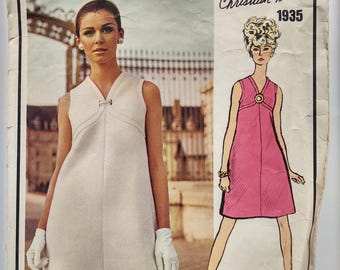May include: A vintage Vogue Paris Original magazine cover. It features a woman in a white dress and a fashion illustration of a pink dress. The text reads "Vogue Paris Original" and "Christian Dior 1935". A fashion advertisement.