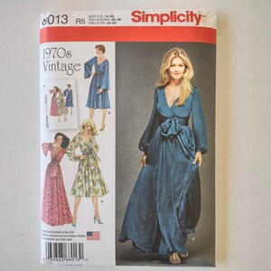Puede incluir: Un sobre de patrón de costura Simplicity, número 8013, con diseños de vestidos vintage de los años 70. La portada muestra ilustraciones de tres estilos de vestidos diferentes, incluyendo un vestido cruzado azul verdoso de manga larga.