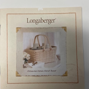 May include: An image of a Longaberger product, a whitewashed medium market basket. The basket, with a handle, is filled with items. The image is set against a cream background, with the Longaberger logo at the top. The text reads 'Whitewashed Medium Market Basket'.