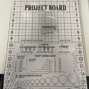 Puede incluir: Un tablero de proyecto blanco con un patrón de cuadrícula, marcas de medición y el texto "PROJECT BOARD". Incluye una guía de tallas de manualidades, diagramas de nudos y círculos de diámetro en milímetros. Empaquetado en plástico transparente con alfileres metálicos.