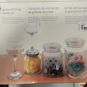 May include: Glass etching starter kit with a wine glass, jars, and etching supplies. The kit includes a wine glass with a mustache design, a jar with yellow candies, a jar with black objects, and a jar with colorful tape.