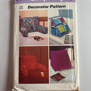 May include: A Simplicity 6011 sewing pattern envelope for a decorator pattern in one size. The front features four images of wedge-shaped pillows and armrest pillows in various fabrics, including floral, plaid, and solid purple textures.
