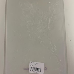 May include: A rectangular, clear plastic embossing folder featuring a debossed floral pattern of cherry blossoms on branches. A white rectangular sticker is attached to the lower centre, displaying the text "Crafter's Companion Emboss'n'Etsy", "C.# 1452", "$0.00", and a barcode with the number "115706".
