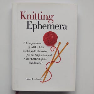 May include: A book titled "Knitting Ephemera" with a red yarn ball and knitting needles illustration. The cover includes text: "A Compendium of ARTICLES, Useful and Otherwise, for the Edification and AMUSEMENT of the Handknitter" by Carol J. Sulcoski.