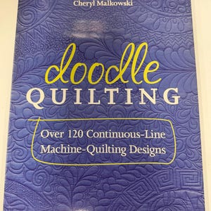 May include: A softcover book titled Doodle Quilting by Cheryl Malkowski with a blue cover featuring embossed continuous-line quilting patterns. The text reads: doodle QUILTING, Over 120 Continuous-Line Machine-Quilting Designs, Cheryl Malkowski.