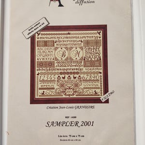 Peut inclure: Un kit de point de croix pour sampler avec un motif détaillé comprenant des lettres, des chiffres et des bordures décoratives. Le kit affiche le texte "SAMPLER 2001" et indique des dimensions de 75 cm x 75 cm pour le lin et 60 cm x 60 cm pour la broderie.