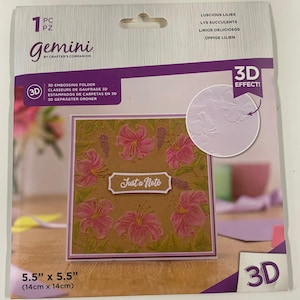 May include: A Gemini 3D embossing folder featuring a floral design with the text "Just a Note." The package is 5.5" x 5.5" and includes the words "Luscious Lilies." The 3D effect is highlighted.