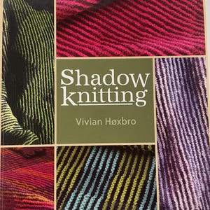 May include: A book cover titled "Shadow Knitting" by Vivian Høxbro. The cover features a collage of colorful knitted fabric swatches in shades of green, pink, purple, and blue. The text is in white on a green background.