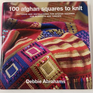 Könnte beinhalten: Ein Buch mit dem Titel "100 afghan squares to knit" mit farbenfrohen gestrickten afghanischen Quadraten auf dem Cover. Der Titel des Buches und die Autorin, Debbie Abrahams, sind sichtbar. Das Cover zeigt eine Vielzahl von Farben, darunter Rot, Rosa, Blau und Gold.