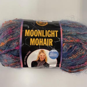 May include: A ball of Moonlight Mohair yarn in shades of blue, pink, and gold. The label features the text "Moonlight Mohair" and a picture of a woman. The yarn is machine washable.