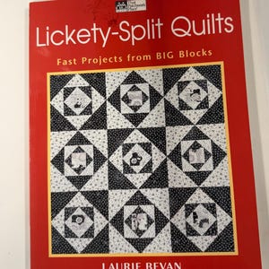 May include: A softcover book titled Lickety-Split Quilts: Fast Projects from BIG Blocks by Laurie Bevan. The cover is bright red with a large central graphic showing a grid of nine black and white patterned quilt blocks with star motifs.