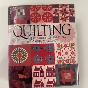Könnte beinhalten: Ein Buch mit dem Titel "QUILTING" und dem Untertitel "Quotations Celebrating An American Legacy". Das Cover zeigt ein Patchwork-Design in Rot-, Rosa- und Burgundertönen mit verschiedenen Quiltblockmustern.