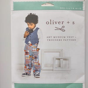 May include: A sewing pattern package featuring a young child wearing an art museum vest and trousers. The package has the text "oliver + s" and "ART MUSEUM VEST + TROUSERS PATTERN". The child is wearing a blue vest, patchwork trousers, and black sneakers.