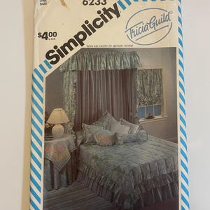 Może przedstawiać: Koperta z wykrojem krawieckim Simplicity 6233 autorstwa Tricia Guild przedstawiająca zestaw do sypialni z łóżkiem z baldachimem, narzutą z falbanami i pasującym obrusem. Biała papierowa koperta ma niebieskie ukośne paski i zawiera żółte kalkomanie.