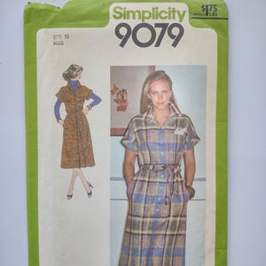May include: Vintage Simplicity 9079 sewing pattern. The pattern shows a woman in a plaid dress with short sleeves and a belt. The envelope is green and white, with the text "Simplicity 9079".