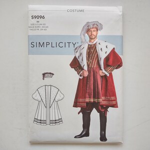 Puede incluir: Un sobre de patrón de costura de disfraz Simplicity S9096 con una fotografía de una persona vistiendo una túnica roja, una capa de piel sintética blanca con manchas negras y un sombrero con plumas. Incluye un dibujo lineal del conjunto.