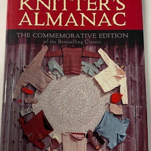 May include: A hardcover book titled Elizabeth Zimmermann's Knitter's Almanac: The Commemorative Edition of the Bestselling Classic. The cover features a circular white lace doily surrounded by various knitted garments in red, blue, and beige.