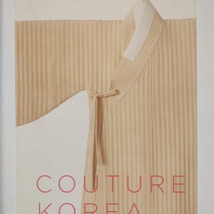 May include: A book cover featuring a beige Korean traditional garment with vertical pleats. The garment has a white collar and tie. The words "COUTURE KOREA" are printed in pink.