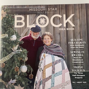 Könnte beinhalten: Das Cover eines Patchwork-Magazins, "Missouri Star Quilt Co. BLOCK Idea Book", zeigt ein Paar mit einem Quilt. Der Quilt hat ein geometrisches Muster in verschiedenen Farben. Links ist ein Weihnachtsbaum.