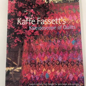 May include: A hardback book titled Kaffe Fassett's Kaleidoscope of Quilts, featuring twenty designs from Rowan for patchwork and quilting. The cover displays a vibrant, diamond-patterned quilt in shades of pink, purple, and red.