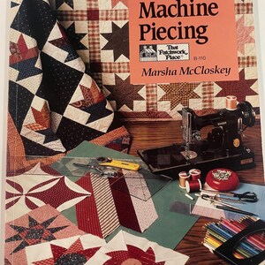 Könnte beinhalten: Ein Buch mit dem Titel "Lessons in Machine Piecing" von Marsha McCloskey, mit einer Singer-Nähmaschine, Quiltwerkzeugen und Stoffmustern. Das Cover zeigt einen Patchwork-Quilt mit Sternmustern. Verschiedene Nähutensilien sind verstreut.