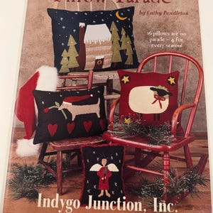 May include: A craft book titled Pillow Parade by Cathy Pendleton featuring 16 pillow designs. The cover displays four decorative pillows with applique motifs including a winter cabin, a sheep, a dog with a flower, and an angel on chairs.
