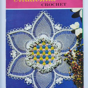 May include: A vintage crochet pattern book titled "Madonna Crochet" with a large, white, crocheted flower design on the cover. The cover is blue and pink, with the number 2 in the upper right corner. The flower has a center of small, colorful crocheted flowers.