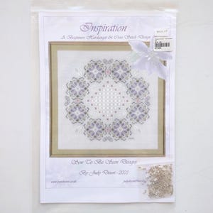 May include: A cross stitch and Hardanger embroidery pattern kit titled Inspiration by Sew To Be Seen Designs. The package includes a printed instruction sheet with a floral-inspired geometric design in shades of purple and grey, plus a small bag of beads.