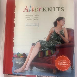 May include: A hardback book titled AlterKNITS: Imaginative Projects and Creativity Exercises by Leigh Radford. The cover features a person knitting in a red leather armchair, a bucket of yarn, and a badge stating AlterKNITS CREATIVITY NOTEBOOK INCLUDED.