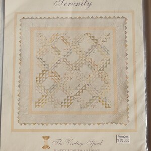 Könnte beinhalten: Ein Quiltmuster mit dem Titel "Serenity" von Verna Mosquera. Das Design zeigt ein zentrales Quadrat mit komplizierten geometrischen Mustern in sanften Pastellfarben. Die Verpackung ist mit "The Vintage Spool" gekennzeichnet.