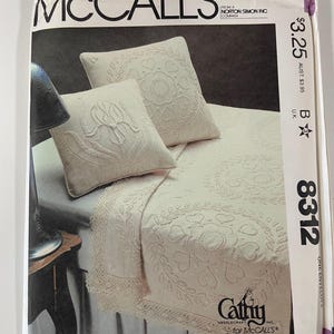 Op de afbeelding: Een vintage McCall's naaimodellenvelop. De envelop toont een crèmekleurige sprei en kussenset met bloemenborduurwerk. Het patroonnummer is 8312. De merknaam "Cathy Needlecraft for McCall's" is zichtbaar.
