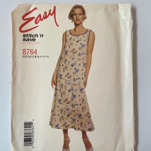Könnte beinhalten: Eine McCall's Schnittmusterhülle für ein Easy stitch 'n save Kleid, Modell 8764, Größe A 8-10-12-14. Die Hülle zeigt ein Foto eines ärmellosen, bodenlangen beigen Kleides mit blauem und violettem Blumenmuster und einem dunklen Saum.
