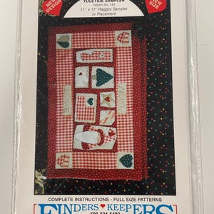 May include: A Yuletide Sampler pattern packet. The design features a red and white gingham pattern with appliqued shapes and the words "LOVE" and "NOEL". The packet is 28 x 43 cm and includes complete instructions.