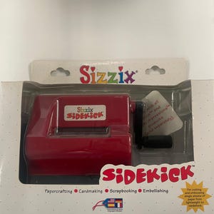 May include: A red Sizzix Sidekick die-cutting and embossing machine in its original packaging. The packaging features the Sizzix logo and the words "Sidekick", "Papercrafting", "Cardmaking", "Scrapbooking", and "Embellishing".