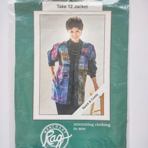 May include: A sewing pattern package titled Take 12 Jacket by Merchant & Mills. The packaging features a photograph of a jacket with a multi-colored patchwork design in shades of blue, purple, and green, worn over a black top and pants.