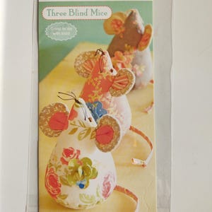 Puede incluir: Se muestran tres ratones de tela con estampados florales y orejas rosas. El empaque indica "Three Blind Mice" y "Great to do with kids!", lo que sugiere un kit de manualidades para niños. La marca "FIG TREE threads" también es visible.