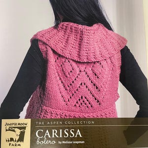 May include: A pink knitted bolero with a ruffled collar and a detailed chevron pattern on the back. The bolero is part of "The Aspen Collection" and is designed by Melissa Leapman. The Juniper Moon Farm logo is visible in the lower left corner.