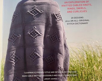 Könnte beinhalten: Buchcover "Continuous Cables" mit einer Frau, die einen grauen Strickschal mit geometrischen Kabelmustern trägt. Das Buch beschreibt gestrickte Knoten, Ringe, Wirbel und Locken. Der Autor ist Melissa Leapman.
