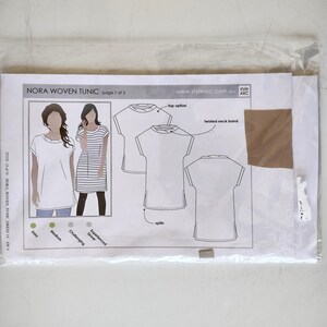 Peut inclure: Un patron de couture pour une tunique tissée Nora dans une pochette en plastique transparent. L'insert en papier présente des illustrations de la tunique, un col torsadé, des fentes latérales et une option haut. Texte : NORA WOVEN TUNIC, page 1 of 3.