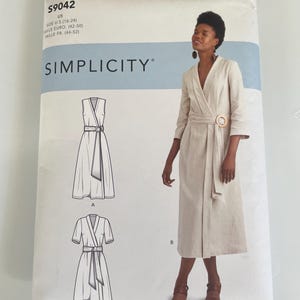 Op de afbeelding: Een Simplicity naaipatroon envelop S9042 voor een wikkeljurk in de maten 42-50. De verpakking bevat illustraties van drie jurkvariaties en een foto van een beige, halflange wikkeljurk met driekwartmouwen en een ronde gesp als detail.
