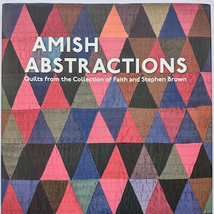 以下が含まれることがあります： 「AMISH ABSTRACTIONS Quilts from the Collection of Faith and Stephen Brown」というタイトルのブックカバー。背景には、黒、ピンク、青、オレンジ、緑の色合いの三角形が繰り返されるパターンがあり、ステッチのラインがはっきりと見えています。