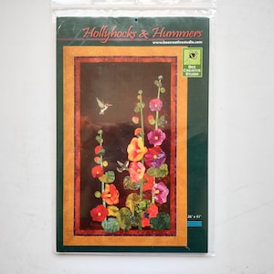 May include: A quilt pattern packet titled Hollyhocks & Hummers by Bee Creative Studio. The cover features a dark background with colorful hollyhock flowers and two hummingbirds. The border is orange and red. Dimensions are 26 inches by 41 inches.
