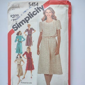 May include: Vintage Simplicity sewing pattern packet showing a woman in a floral dress. The packet includes illustrations of different dress styles and the text "Simplicity" and "5434".