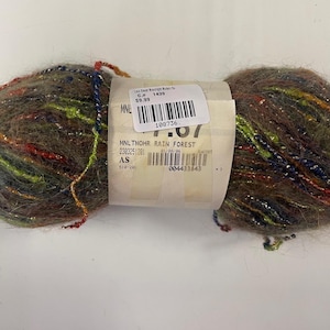 May include: A ball of yarn in shades of brown, green, red, and blue. The yarn has a soft, fuzzy texture and is wrapped with a paper label. The label includes a barcode and the text "MNLTHOHR RAIN FOREST".