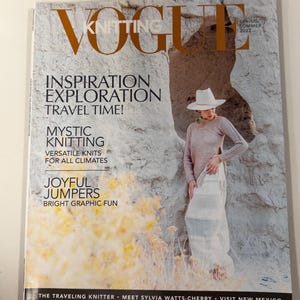 Op de afbeelding: Vogue Knitting voorjaar/zomer 2022 tijdschriftomslag met de tekst Inspiration Exploration Travel Time, Mystic Knitting en Joyful Jumpers. De omslag toont een persoon in een lichtgekleurde trui en hoed voor een rotsformatie.