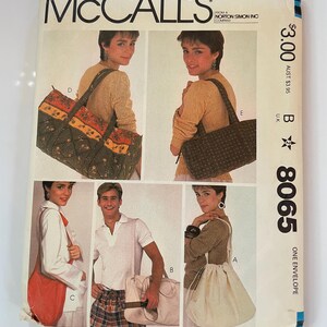 Op de afbeelding: Een McCall's 8065 naaipatroon-envelop met illustraties van vijf verschillende tasstijlen. De ontwerpen omvatten een doorgestikte reistas, een donkere tas met patroon, een effen rode schoudertas, een lichte rechthoekige tas en een tas met trekkoord.