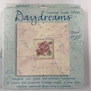 Pode incluir: Um kit de ponto cruz contado com um desenho de rosa emoldurado. O kit inclui um tapete de design, vidro e bordado. A embalagem é azul clara com as palavras "Daydreams" e "Real Glass!". O design finalizado mede 20 cm x 20 cm.
